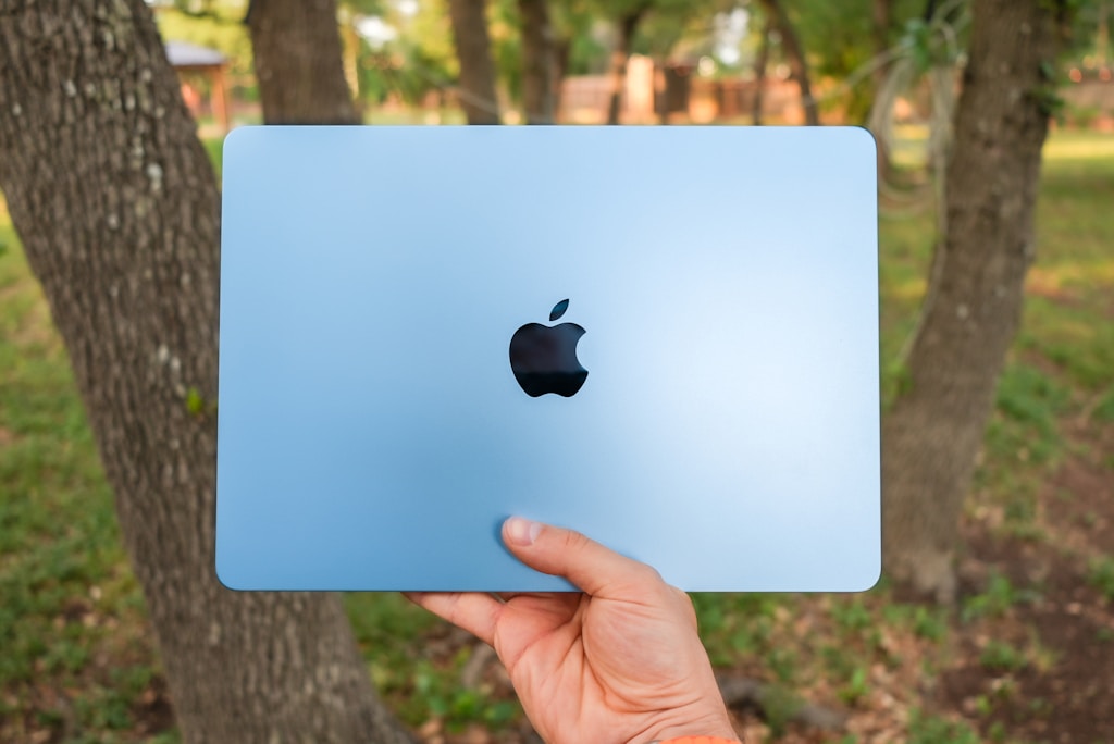 sky blue macbook air being held up outside